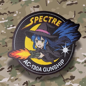 May include: A circular patch featuring an anime-style witch with blue hair, wearing a black hat with a pink band, and holding a gun that is firing flames. The patch has the text "SPECTRE" and "AC-130A GUNSHIP".