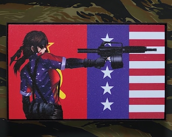 May include: A rectangular patch featuring an anime-style character aiming a machine gun. The patch is divided into sections with a red and white striped area, a blue area with white stars, and a red area with a yellow star.