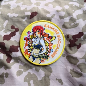 May include: A yellow and white round patch with a cartoon image of a woman with red hair wearing a bikini and holding a gun. The text "KANAME BUCCANEER RECON" is written around the edge of the patch.