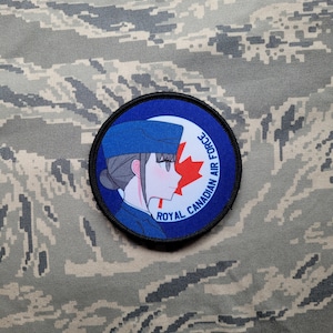Peut inclure: Un écusson brodé bleu et blanc avec une femme de dessin animé portant un chapeau bleu et une feuille d'érable rouge. Le texte "Royal Canadian Air Force" est écrit autour du bord de l'écusson.
