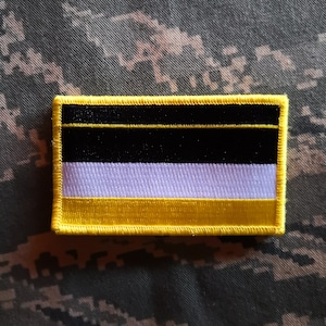 Könnte beinhalten: Ein gestickter Aufnäher in Gelb, Schwarz und Weiß mit gelbem Rand. Der Aufnäher zeigt ein horizontales dreifarbiges Design mit einem dünnen gelben Streifen oben, einem schwarzen Streifen in der Mitte und einem weißen Streifen unten.