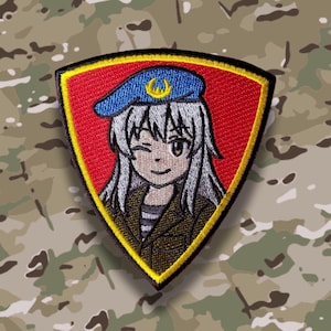 Könnte beinhalten: Gestickter Aufnäher mit einem Anime-Charakter, der zwinkert. Die Figur hat weiße Haare und trägt eine blaue Baskenmütze mit einem goldenen Emblem. Der Aufnäher ist goldfarben umrandet und vor einem roten Hintergrund platziert, mit einem Tarnmuster im Hintergrund.