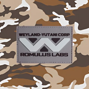 May include: A gray patch with white text and a white logo. The text reads "Weyland-Yutani Corp" and "Romulus Labs". The logo is a stylized "W" with three white triangles.