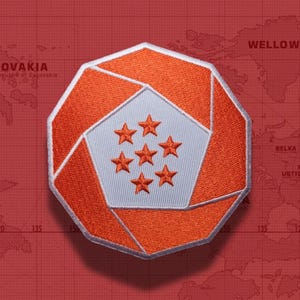 Könnte beinhalten: Ein achteckiger gestickter Aufnäher mit einem leuchtend orangefarbenen Rand und einem geometrischen, blendenartigen Design, das ein hellgraues fünfeckiges Zentrum umgibt. In der Mitte befinden sich sieben kleine, gleichmäßig verteilte orange Sterne.
