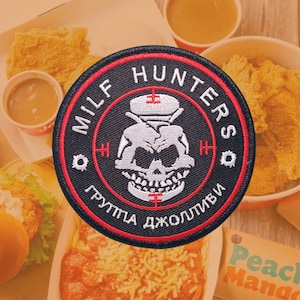 Può includere: Una toppa ricamata di colore rosso, bianco e nero con il testo "MILF HUNTERS ГРУППА ДЖОЛЛИБЫ" e una grafica di un teschio.