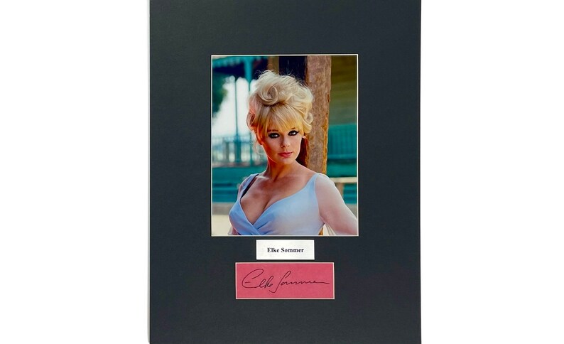 May include: A framed photograph featuring a woman with blonde hair and a light blue dress. The photo is matted in black and includes a nameplate that reads "Elke Sommer" and a signed autograph.
