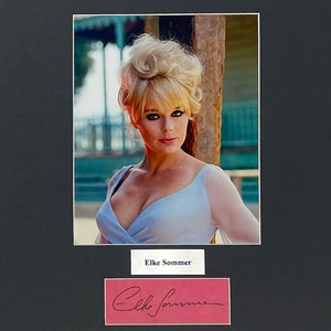 May include: A framed photograph featuring a woman with blonde hair and a light blue dress. The photo is matted in black and includes a nameplate that reads "Elke Sommer" and a signature.