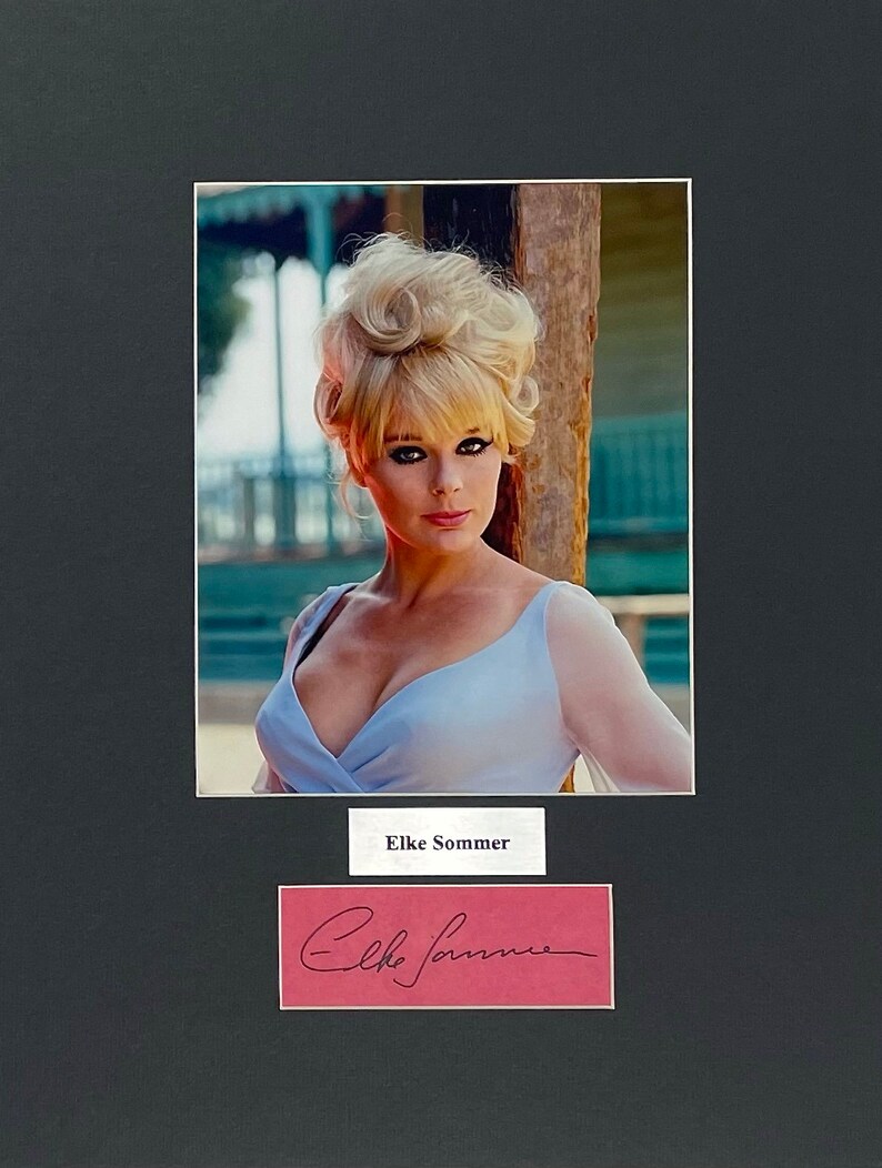 May include: A framed photograph featuring a woman with blonde hair and a light blue dress. The photo is matted in black and includes a nameplate that reads "Elke Sommer" and a signature.