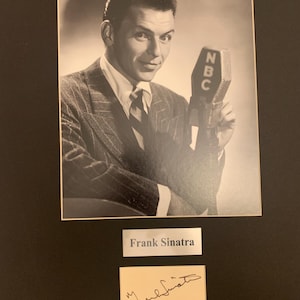 May include: Black and white photograph of Frank Sinatra holding an NBC microphone. He is wearing a suit and tie. Below the photo are two smaller cards, one with his name and the other with his signature.