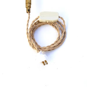 May include: A beige electrical cord with a white inline switch and a white plug. The cord is coiled and the plug is at the bottom of the image.