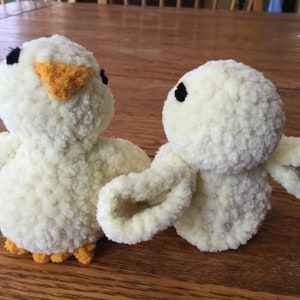 May include: Two handmade, plush yellow chick toys with black eyes and orange beaks and feet. The soft, fluffy chicks are positioned facing each other, suggesting a friendly interaction. The toys are likely made of a soft, textured yarn.