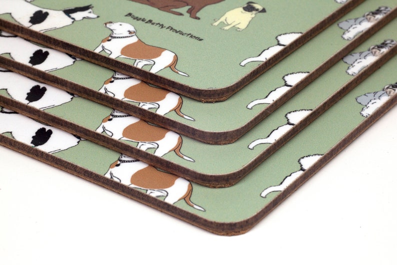 May include: A set of four green coasters with a brown border. Each coaster features a different cartoon dog breed, including a pug, a bulldog, and a husky. The coasters are stacked on top of each other, with the top coaster showing a bulldog. The text "Buggle Berry Productions" is printed on the coaster.