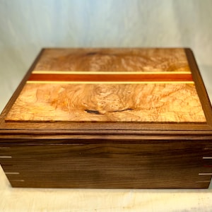 May include: A wooden box with a burl wood top and a walnut wood base. The top has a thin red and white inlay.