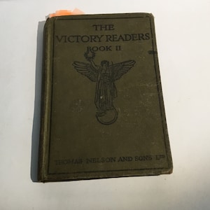 Puede incluir: La portada de un libro verde titulado "The Victory Readers Book II" con una ilustración de una figura alada sosteniendo una corona.