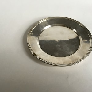 May include: A silver charger plate with a raised rim and a smooth, reflective surface.