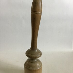 May include: A wooden mallet with a long, slender handle and a rounded head. The handle is smooth and has a slight taper. The head is slightly wider than the handle and has a rounded top.