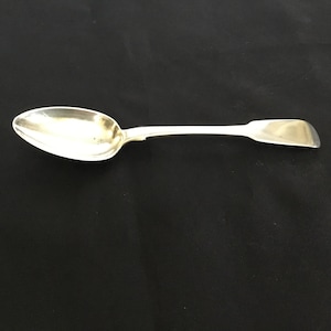 May include: A silver spoon with a rounded bowl and a long, slender handle. The spoon is polished and shiny.