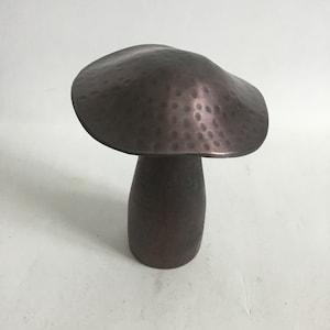 May include: A hammered copper mushroom sculpture with a rounded top and a cylindrical base.