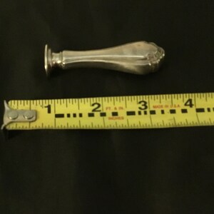 Op de afbeelding: Een zilveren zegel met een decoratief handvat. De zegel is ongeveer 7,6 cm lang.