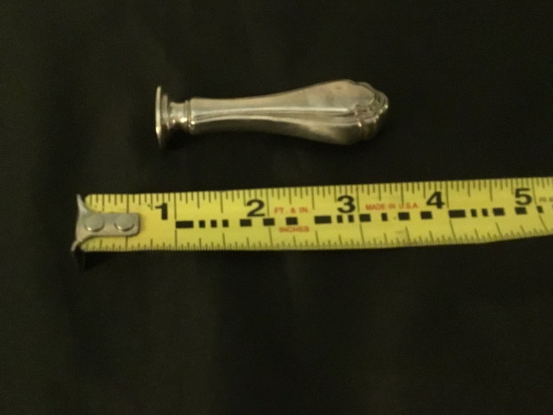 Op de afbeelding: Een zilveren zegel met een decoratief handvat. De zegel is ongeveer 7,6 cm lang.