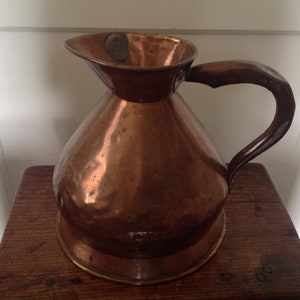 May include: A copper pitcher with a hammered finish and a curved handle. The pitcher has a wide mouth and a rounded base.