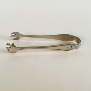 May include: Silver sugar tongs with a decorative design on the handle.