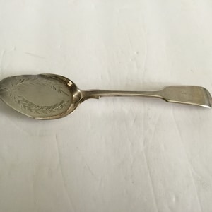May include: A silver cake server with an ornate design on the front of the spoon. The handle is plain and the spoon is slightly curved.