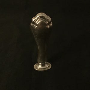 Op de afbeelding: Een zilveren zegel met een decoratieve, geribbelde bovenkant en een ronde basis.