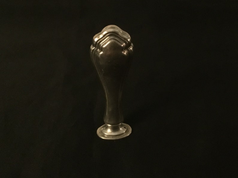 Op de afbeelding: Een zilveren zegel met een decoratieve, geribbelde bovenkant en een ronde basis.