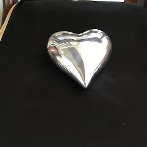 May include: A silver heart-shaped box on a black background.