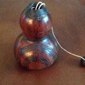 May include: A brown gourd with black markings and a string attached to a small black bead. The gourd has a small opening at the top.