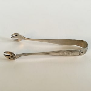 Könnte beinhalten: Silberne Zuckerzange mit einem dekorativen Design am Griff.