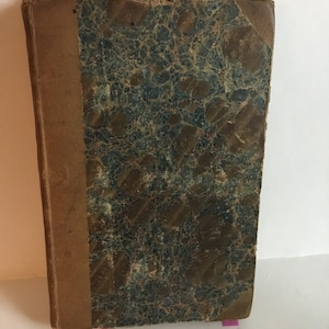 Könnte beinhalten: Ein altes braunes Buch mit einem marmorierten Einband. Das Buch hat einen Rücken mit einem Etikett und ist in braunes Leder gebunden.