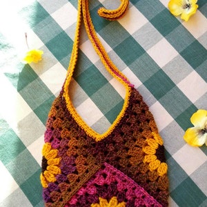 May include: A crocheted bag with a long strap. The bag is made of brown, pink, and yellow yarn and features a sunflower design.