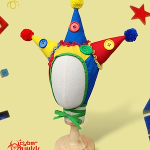 May include: A colorful jester hat with blue, red, and yellow cone-shaped points, each adorned with a pom-pom and button. The hat features a green trim and a green bow at the base. The hat is displayed on a mannequin head.