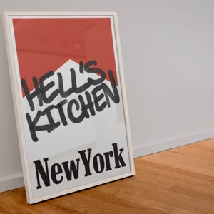 May include: A white framed poster with a red background and black text that reads "Hell's Kitchen New York".