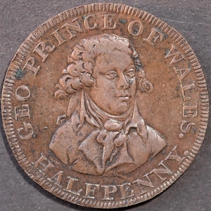 Può includere: Una moneta color rame con il busto di un uomo con capelli ricci e cravatta. La moneta è incisa con "GEORGE PRINCE OF WALES" e "HALFPENNY" sui bordi. La moneta ha un aspetto strutturato e invecchiato.