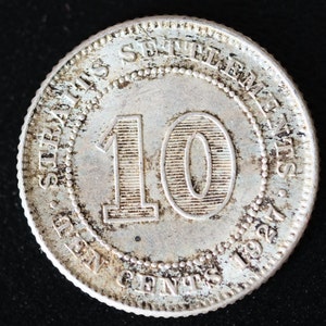 May include: A silver coin with the inscription "STRAITS SETTLEMENTS" and "TEN CENTS 1921" around the edge. The number "10" is in the centre of the coin.