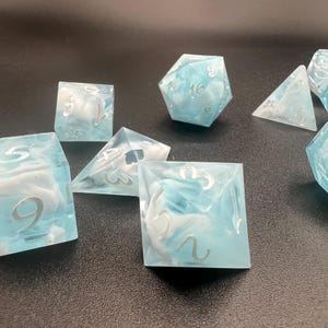 May include: A set of polyhedral dice in various shapes, including a d4, d6, d8, d10, d12, and d20. The dice are a translucent light blue with white swirls and silver numbering. Ideal for tabletop gaming.