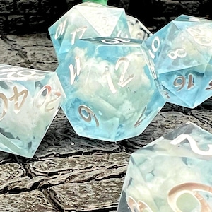 May include: A set of six-sided and multi-sided dice with a blue and white cloudy design. The dice have white numbers and are designed for tabletop role-playing games. The dice are made of a clear, translucent material.