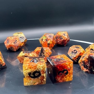 May include: A collection of multi-sided dice in various shapes. The dice are a mix of orange, yellow, and red with black numbering. Some dice are cube-shaped, while others are multi-sided, suitable for tabletop games.