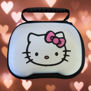 May include: White carrying case with a black handle and zipper. The case features a Hello Kitty design with a pink bow.