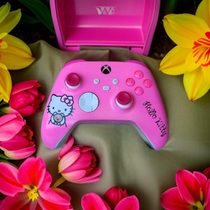 Op de afbeelding: Een roze Xbox-controller met een Hello Kitty-ontwerp. De controller heeft een witte knop en een roze Hello Kitty-personage aan de voorkant.
