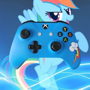 Puede incluir: Un mando Xbox azul con botones negros y un diseño de pony arcoíris. El mando tiene una nube blanca y un rayo en el lado derecho.