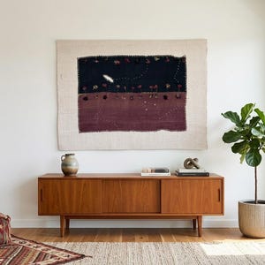May include: A rectangular wall tapestry featuring a dark navy and deep maroon color-blocked design with small embroidered floral motifs, hung above a long, low wooden sideboard with sliding doors and a smooth, warm-toned finish.