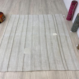 Peut inclure: Un tapis rectangulaire gris clair à rayures verticales et un patch. Un coussin rond coloré et trois tapis roulés de couleurs variées sont également visibles.