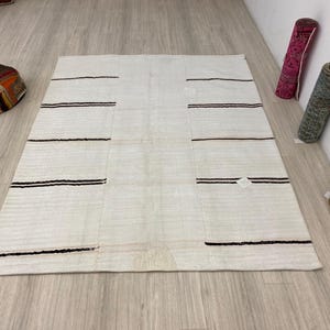 May include: A white woven rug with thin black stripes. The rug has a subtle texture and is made of natural fibers.