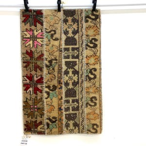 May include: A rectangular, patchwork rug with a beige background and various geometric and floral patterns in shades of brown, red, pink, and green. The rug is hanging from a white rod with black clips.