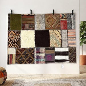 Könnte beinhalten: Ein rechteckiger Wandteppich, der aus verschiedenen Patchwork-Stoffsegmenten in unterschiedlichen Farben wie Olivgrün, Creme, Schwarz, Rot und Braun besteht und geometrische Muster, einfarbige Blöcke sowie gestreifte Texturen aufweist.