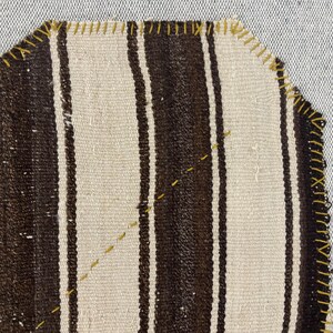 Puede incluir: Una pieza de tela tejida con rayas verticales alternas en marr&oacute;n oscuro y blanco roto. Los bordes est&aacute;n rematados con una puntada de sobrehilado amarilla visible, y una l&iacute;nea diagonal de costura decorativa amarilla cruza el centro del tejido.